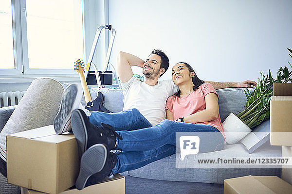 Happy couple sitting on couch surrounded by cardboard boxes