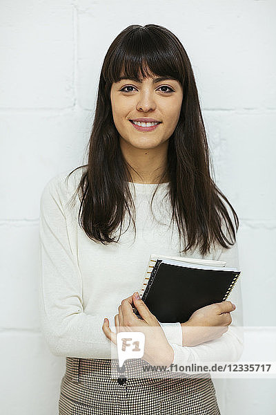 Portrait of smiling young woman with notebook at brick wall