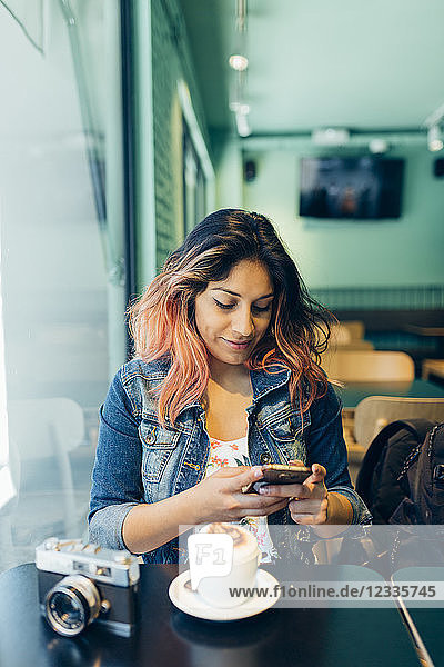 Smiling woman sitting in coffee shop looking at cell phone
