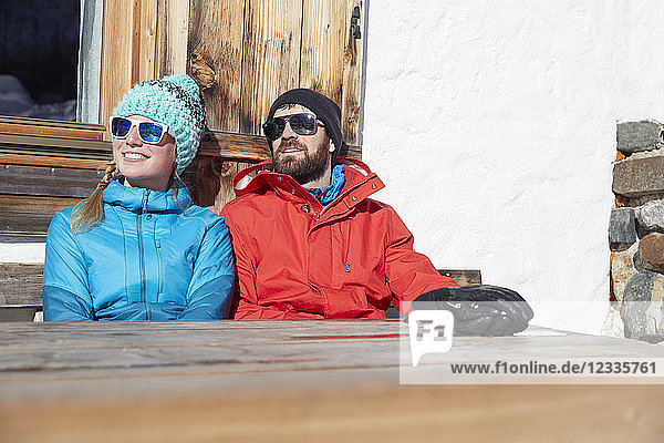 Couple sunbathing in winter at wooden mountain hut