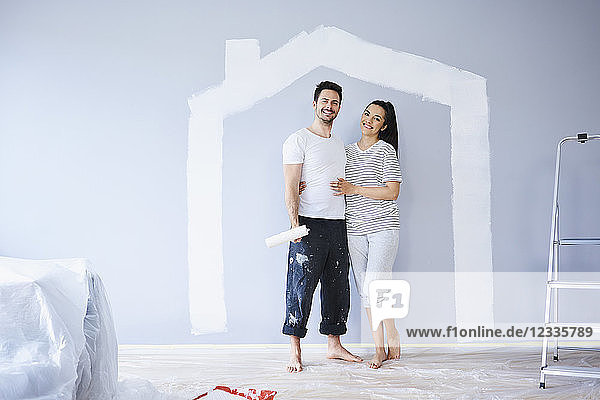 Portrait of happy couple painting in new apartment with house shape on wall