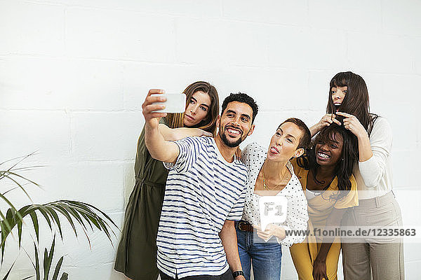 Playful colleagues standing at brick wall taking a selfie