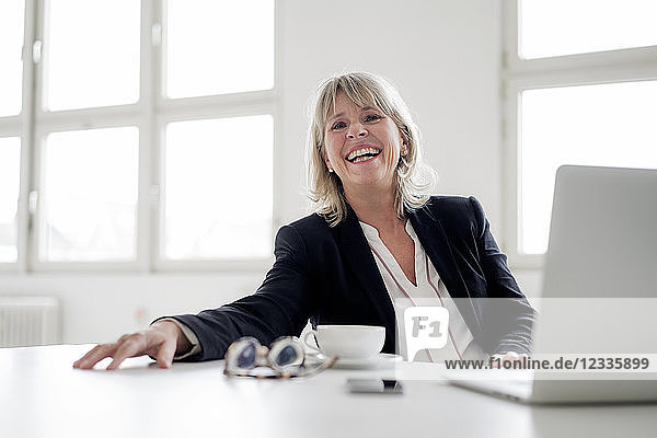 Portrait of laughing mature businesswoman with laptop at desk in the office