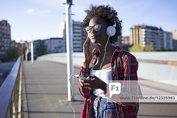 Portrait of young woman on a bridge listening music with headphones