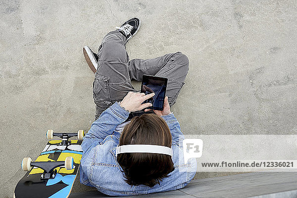 Young man with skateboard sitting on ground  using digital tablet