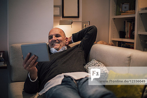 Senior man lying on couch  reading e-book
