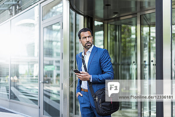 Businessman with smartphone  earphones and laptop bag