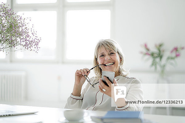 Portrait of happy mature businesswoman holding cell phone at desk