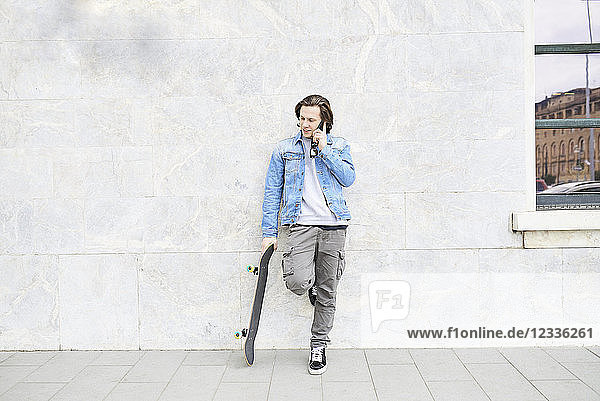 Young man holding skateboard  using smartphone