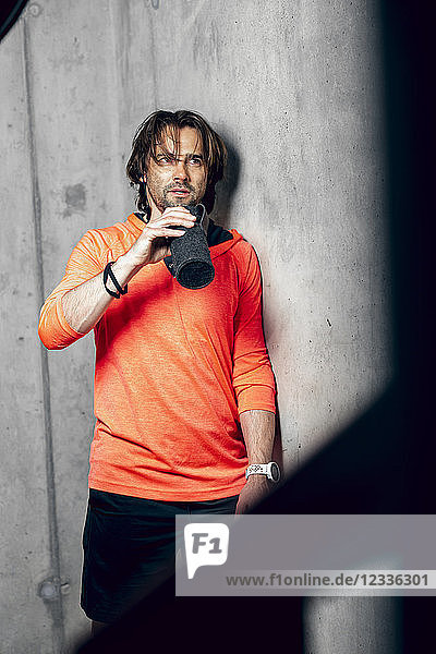 Athlete wearing standing at concrete wall drinking from flask