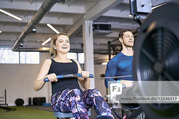 Man and woman at gym exercising together on rowing machines