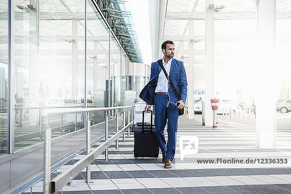 Businessman with trolley and smartphone at airport