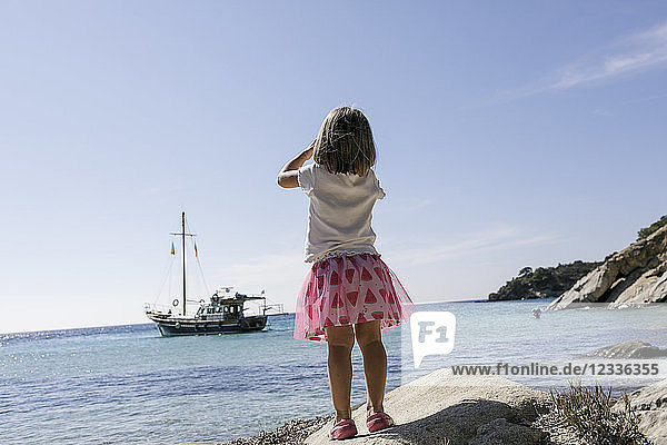Back view of little girl with binoculars watching boat