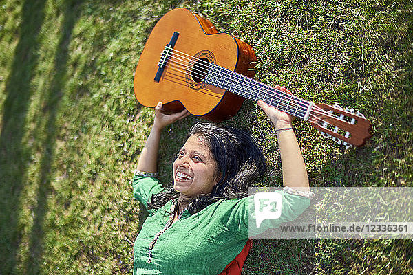 Happy young woman with guitar lying on meadow