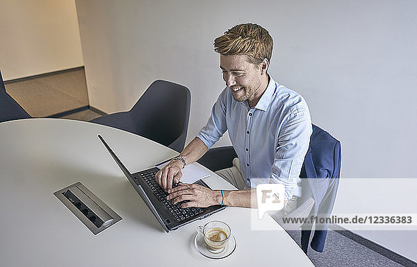 Smiling businessman working on laptop in board room