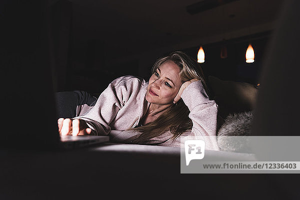 Smiling woman lying on couch at home using laptop