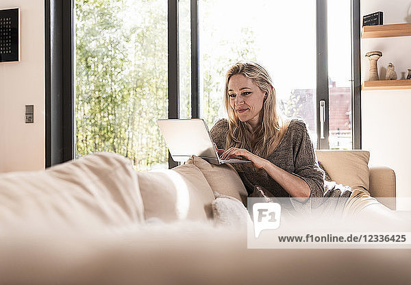 Smiling mature woman sitting on couch at home using laptop