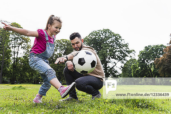 Father playing football with daughter in a park
