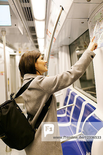 Spain  Barcelona  smiling young woman with backpack looking at map in underground train