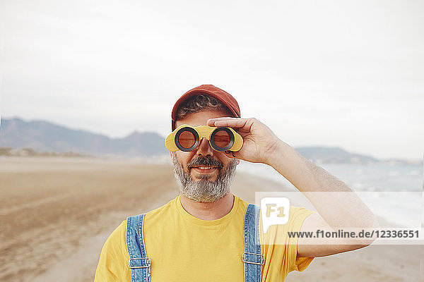 Bearded man using binoculars on the beach