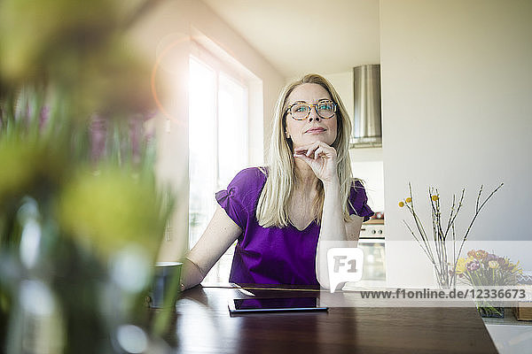 Portrait of pensive woman sitting at table at home
