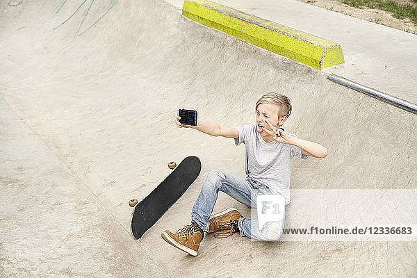 Boy with skateboard taking selfies with smartphone