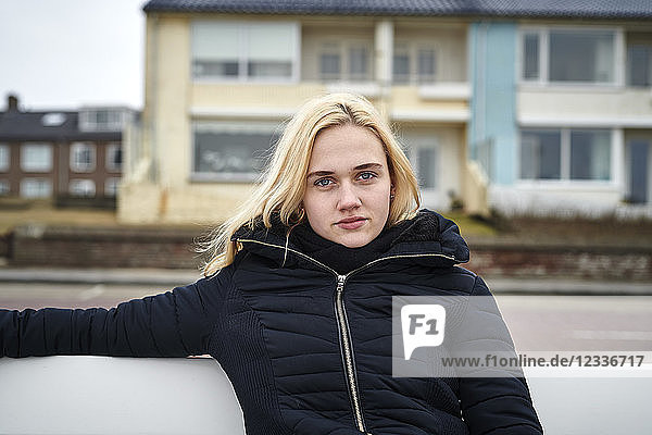 Netherlands  portrait of blond young woman sitting on bench in winter