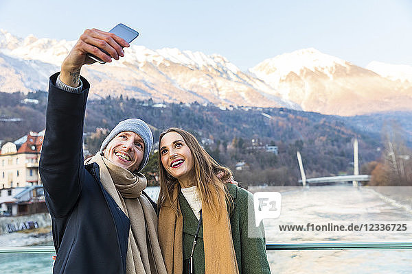 Austria  Innsbruck  portrait of happy young couple taking selfie with smartphone in winter