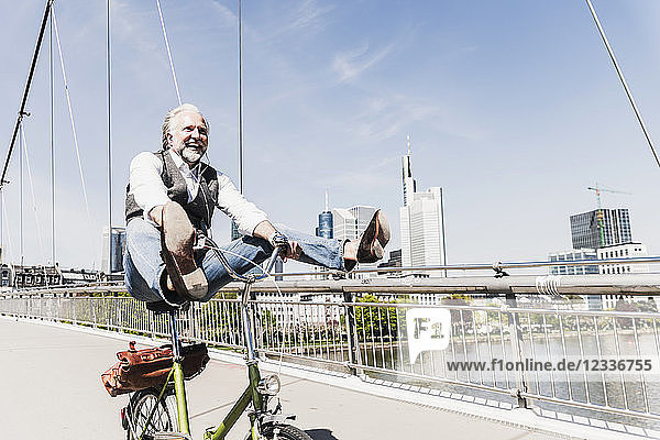 Playful mature man on bicycle on bridge in the city