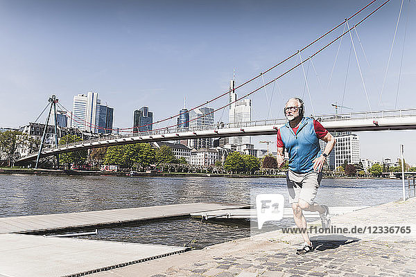 Mature man with headphones running at the riverside in the city