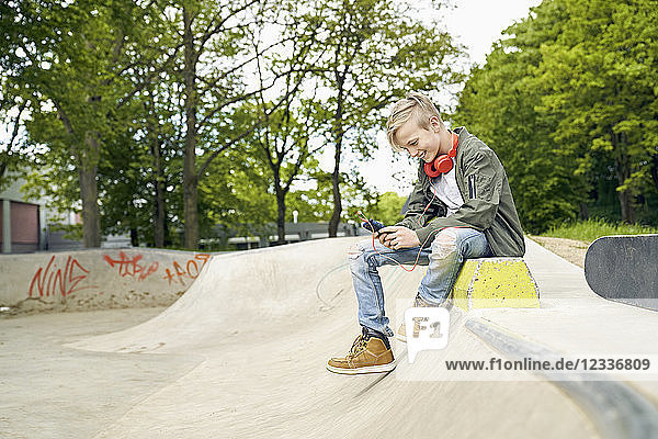 Boy with headphones in skatepark using smartphone
