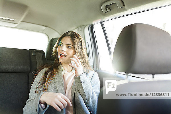 Portrait of young businesswoman on the phone sitting on backseat of a car