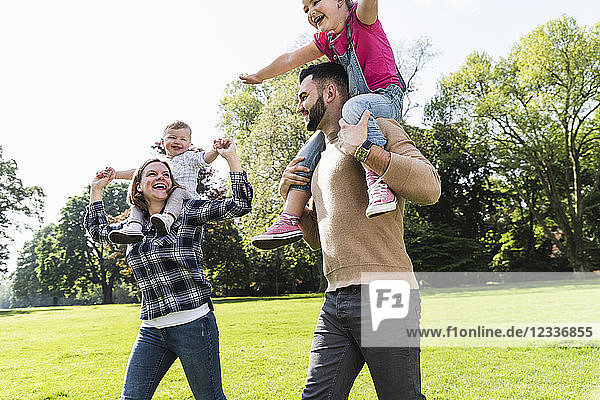 Happy parents carrying children on shoulders in a park