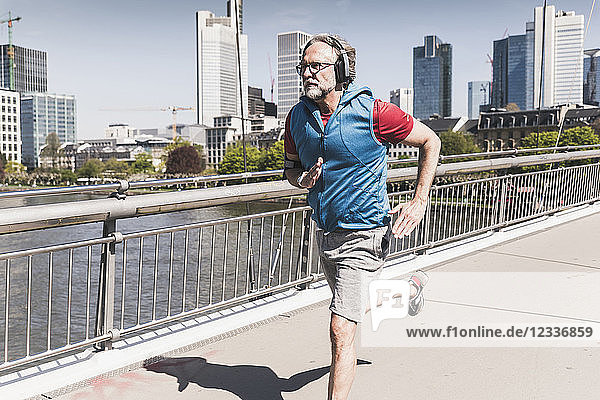 Mature man with headphones running on bridge in the city