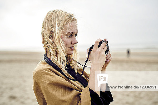 Blond young woman using camera on the beach