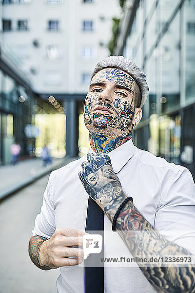 Young businessman with tattooed face  fastening tie