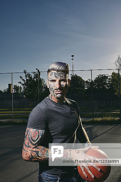 Portrait of tattooed young man with basketball on court