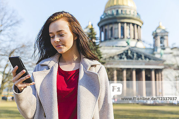 Russia  St. Petersburg  young woman using smartphone in the city