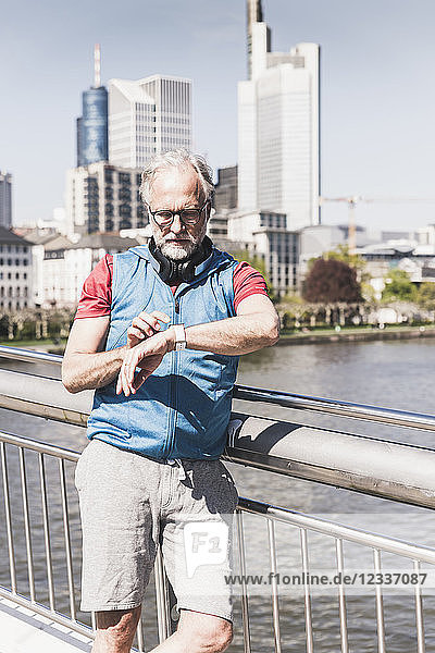 Athletic mature man with headphones taking the time on bridge in the city