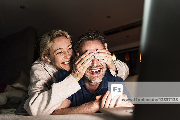 Laughing couple lying on couch with laptop having fun