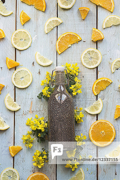 Chia drink in bottle and slice of orange and lemon on wood