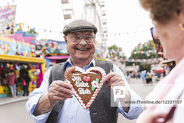 Portrait of happy senior man presenting gingerbread heart on fair
