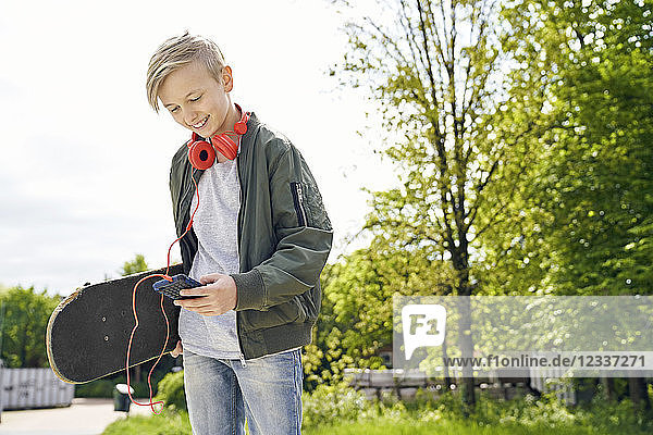 Boy with headphones and skateboard using smartphone
