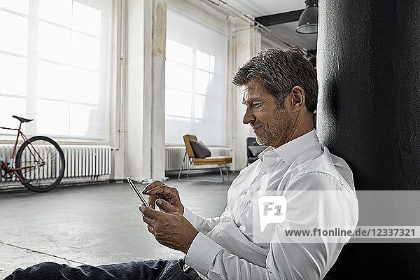 Mature man sitting on the floor using smartphone in loft flat