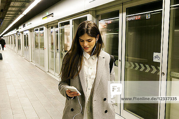 Young woman using cell phone and earphones in a passageway