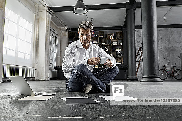 Mature man sitting on ground with laptop and notes in loft