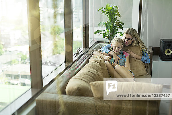 Mother and daughter in modern living room on a couch looking at smartphone together