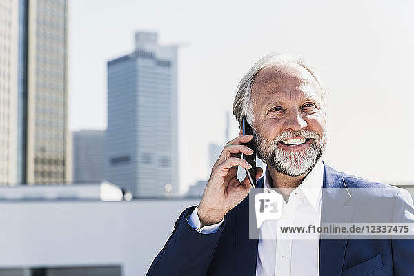 Smiling mature businessman in the city on cell phone