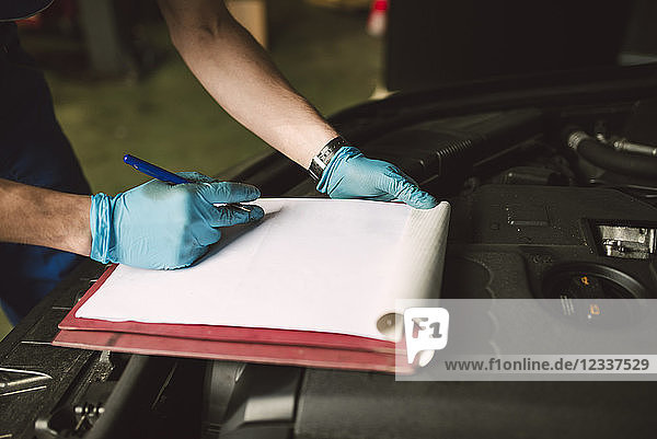 Close-up of mechanic taking notes on clipboard in his workshop