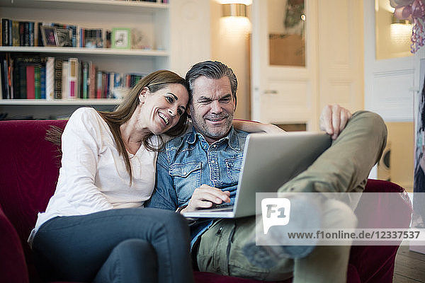 Happy couple sitting on couch using laptop